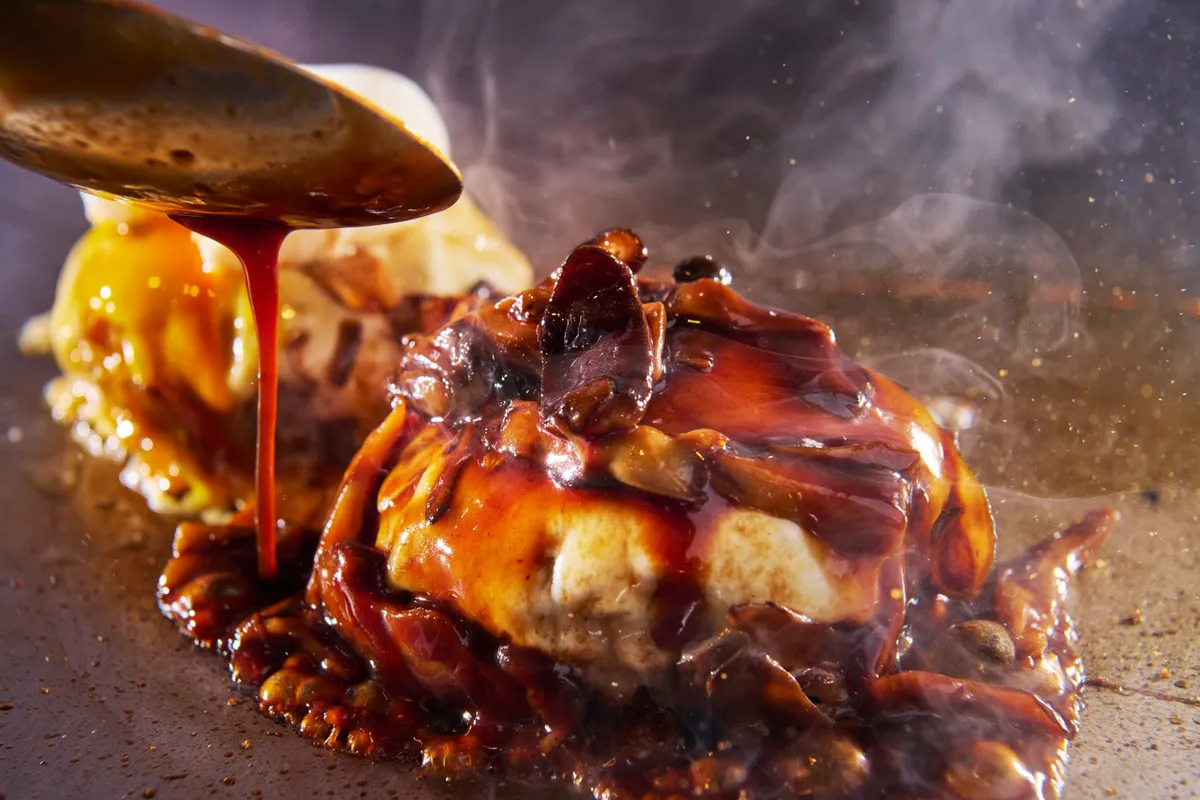 鉄板で焼き上げられるハンバーグにソースがかけられる様子