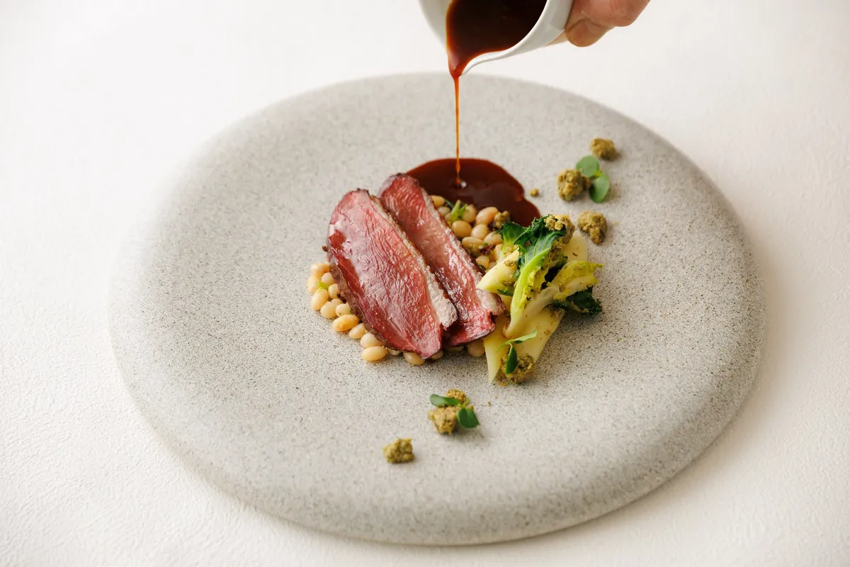 メインディッシュの鴨ローストに芳醇なソースが注がれる様子