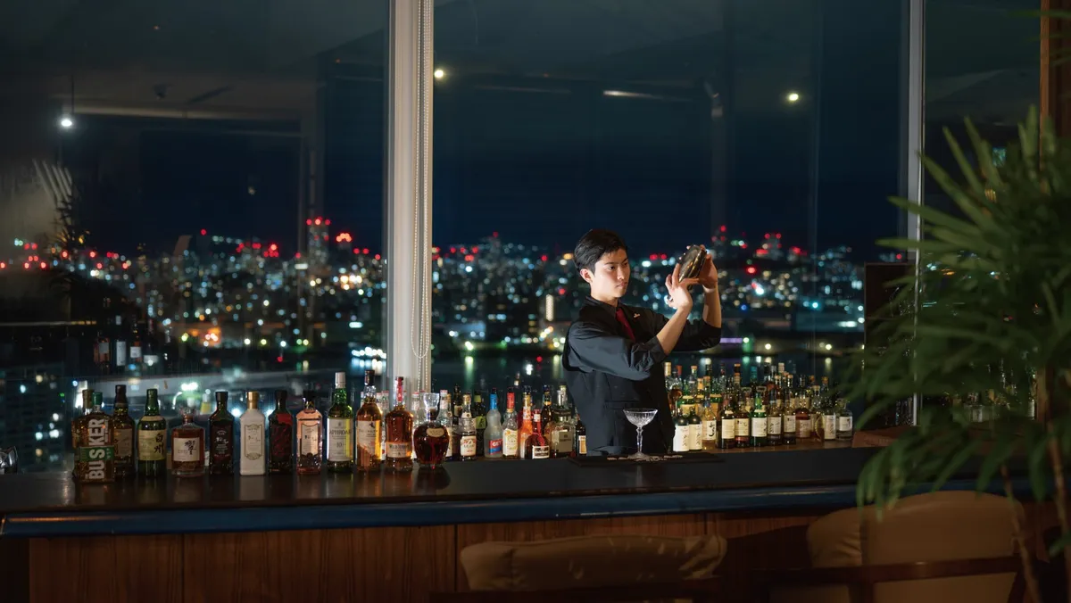 広島の夜景をバックにカクテルを作るバーテンダー