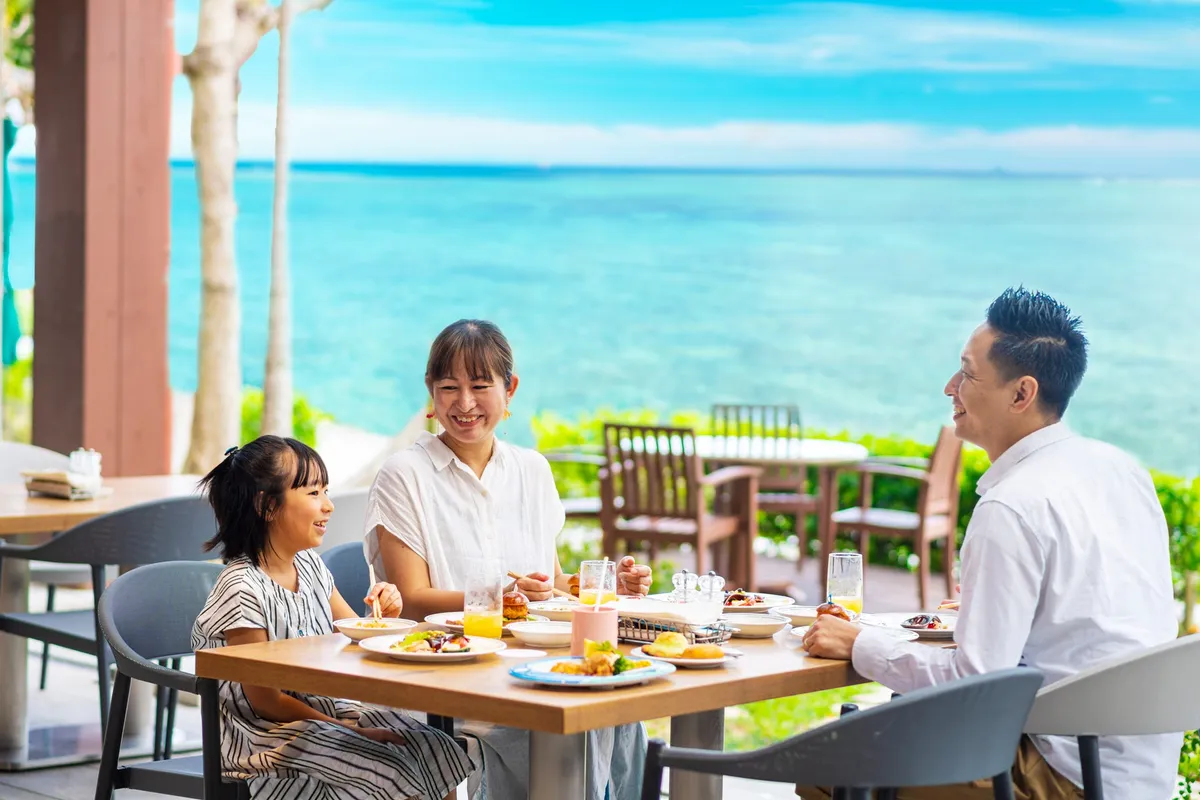 エメラルドグリーンの海を眺めながらテラスで食事を楽しむ家族