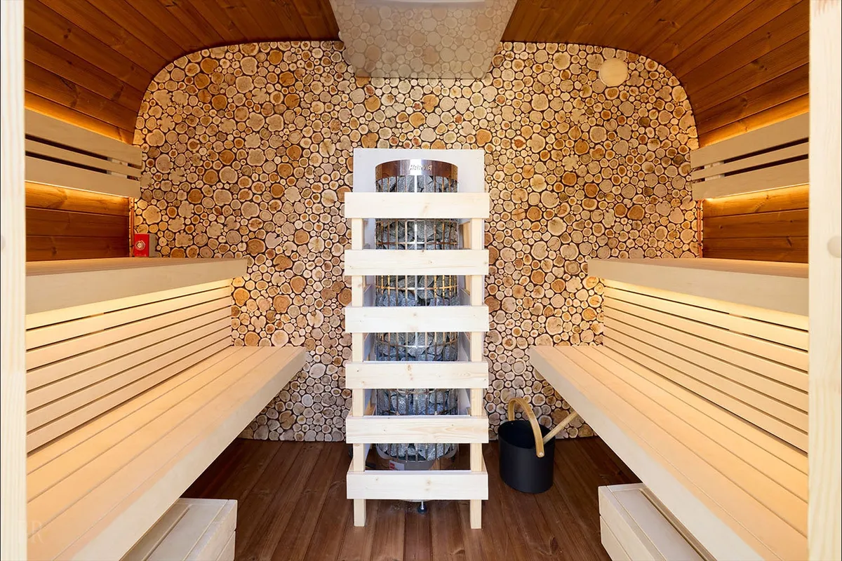 エストニア産サウナの内部。切り出された木材が壁一面に敷き詰められ、本格的な薪ストーブが鎮座します。