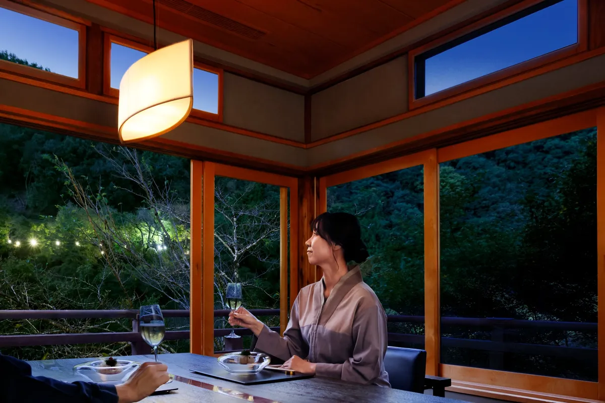 夕暮れ時の窓辺で、奥嵐山の景色を眺めながら夕食を愉しむ女性