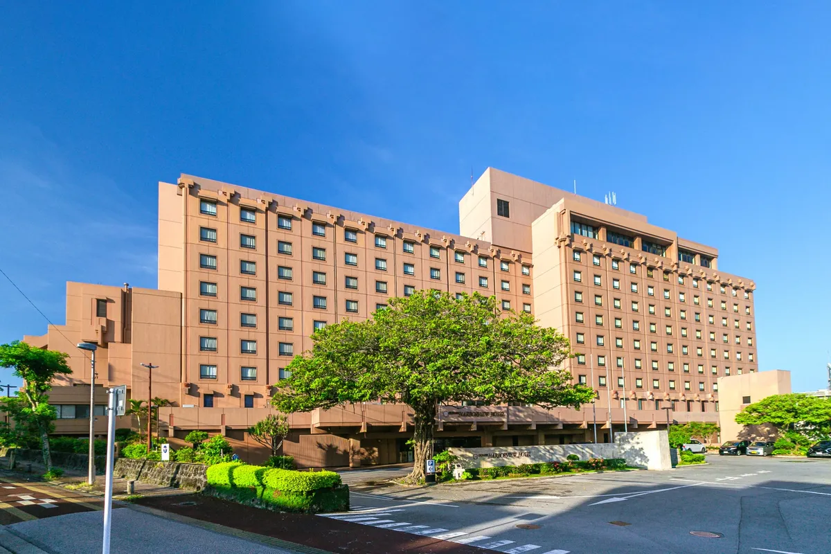 青空の下に佇む、沖縄ハーバービューホテルの格調高い外観とシンボルツリーのガジュマル