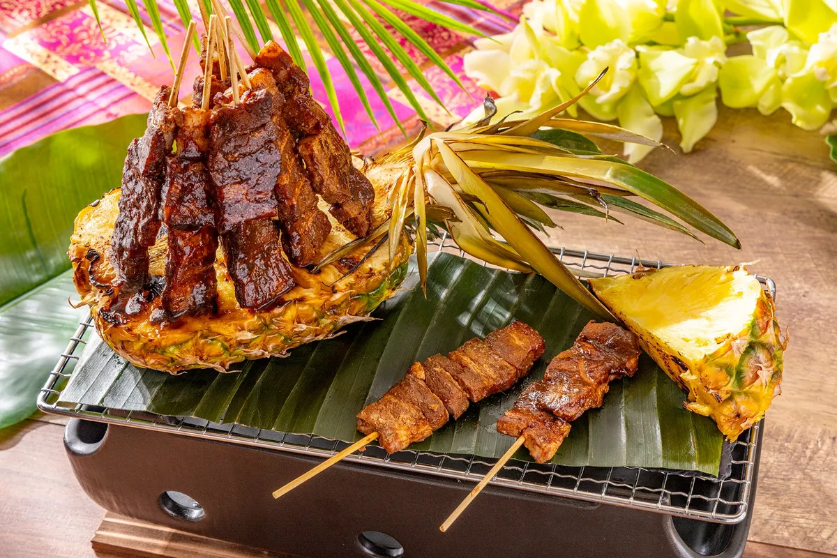 パイナップルに盛り付けられたポークの串焼き