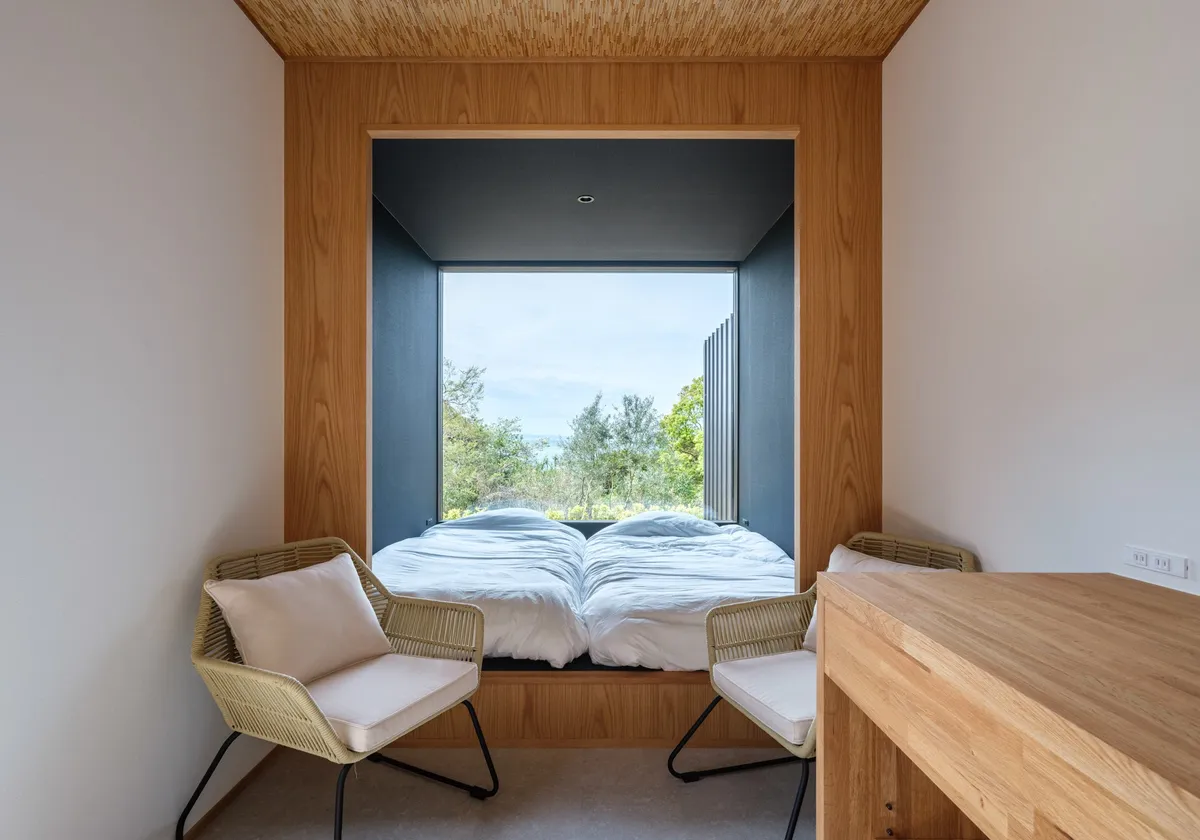 大きな窓から外の緑を絵画のように切り取る落ち着いた寝室