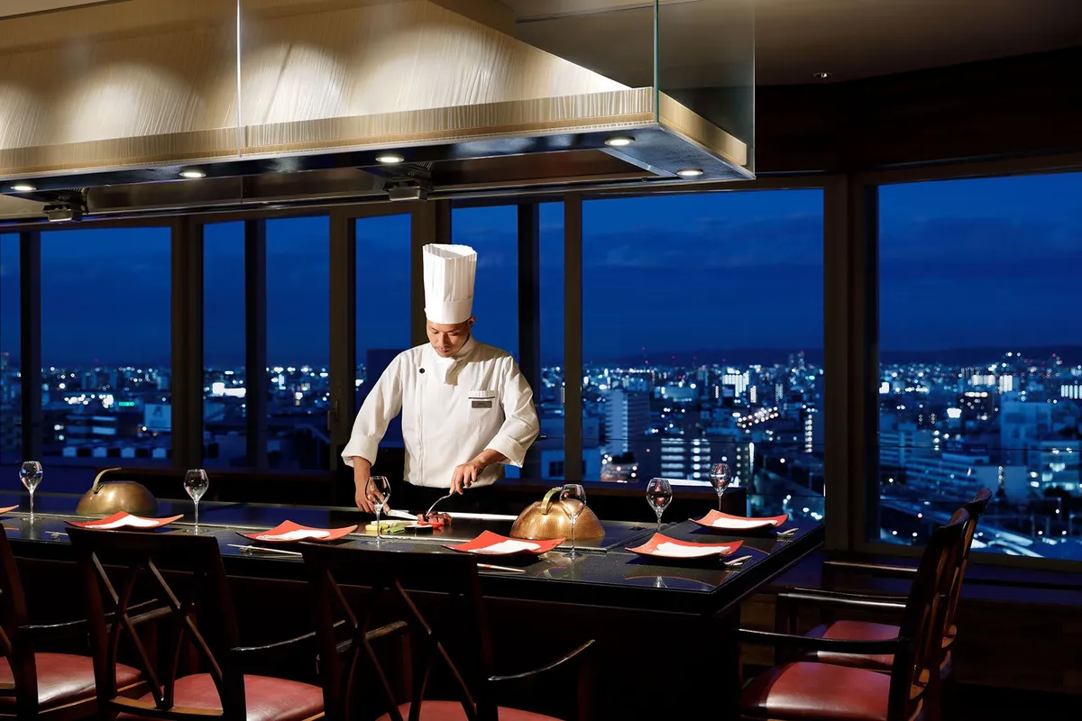 夜景を背景にシェフが調理する鉄板焼きレストランの店内