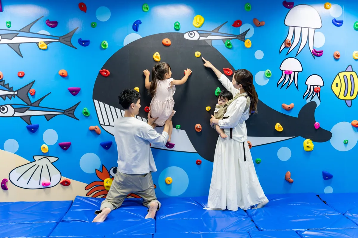 海の生き物が描かれた壁でボルダリングを楽しむ家族