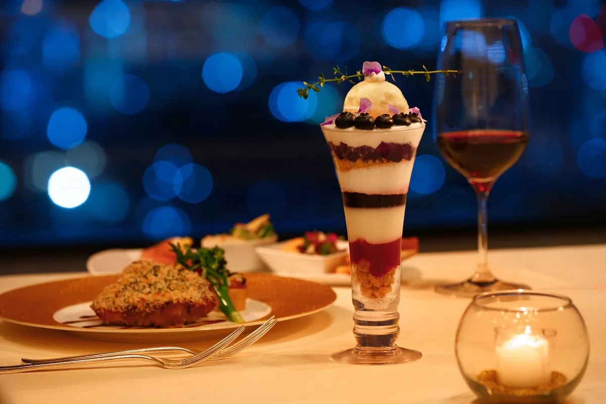 新宿の夜景を背景に輝く夜パフェとディナー料理
