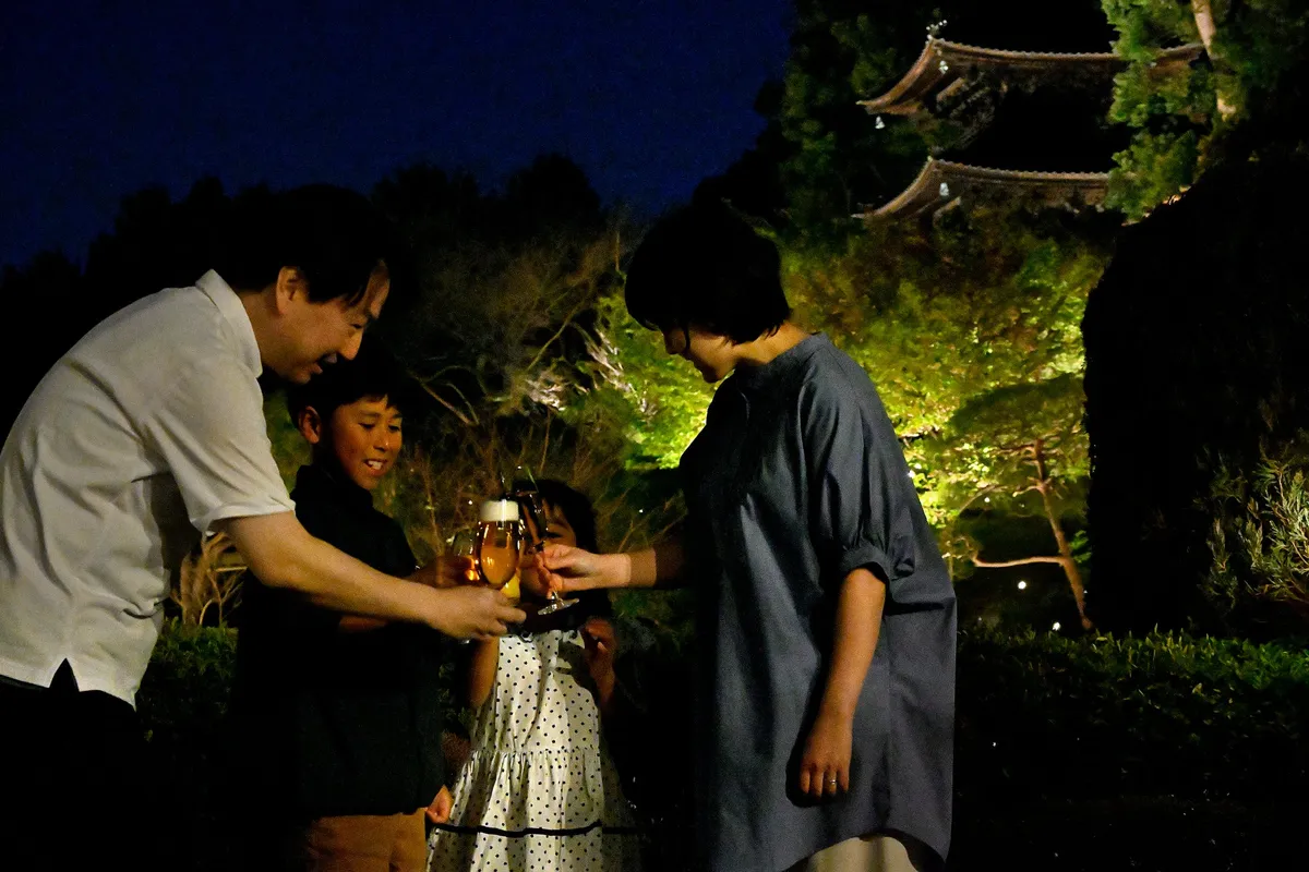 ライトアップされた三重塔を背に夜の庭園で乾杯する家族