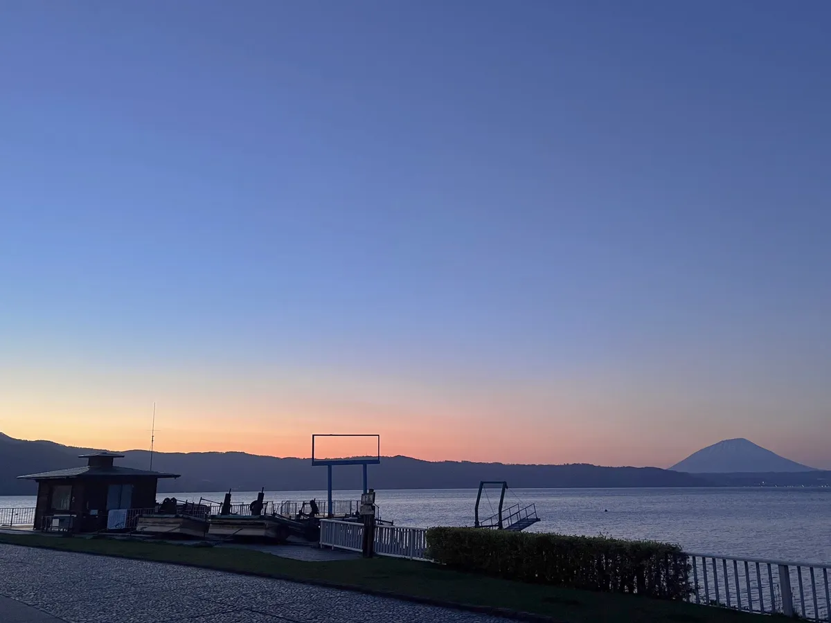 夕焼けに染まる湖畔と遠くに望む羊蹄山のシルエット
