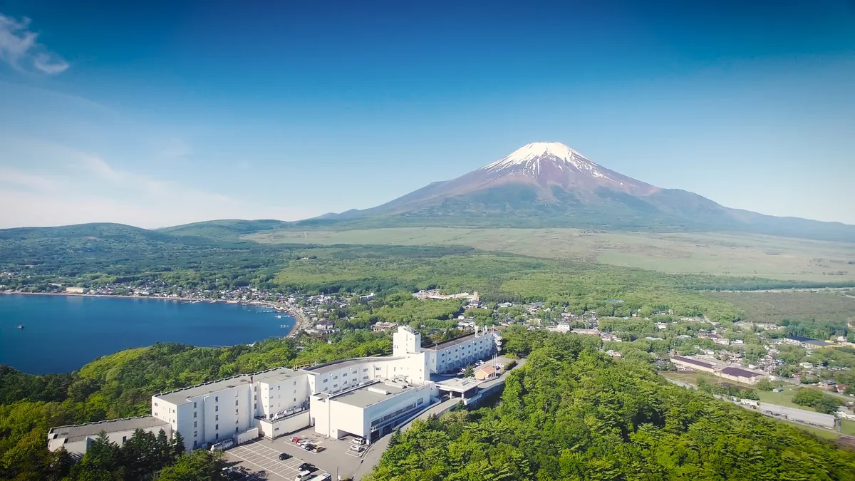 青空の下に広がる山中湖と富士山、緑に囲まれたホテル全景