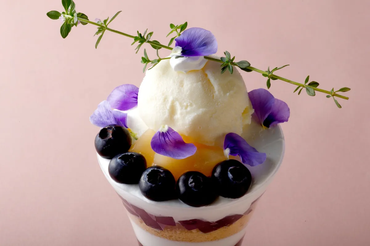 ラベンダー色の花びらとブルーベリーが飾られた華やかなパフェのアップ