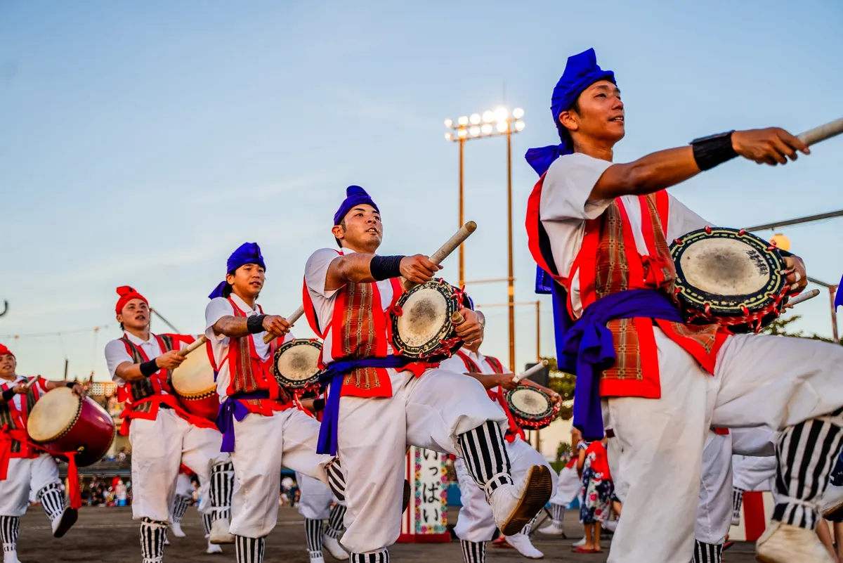 青空の下で力強く太鼓を叩き踊るエイサーのパフォーマーたち