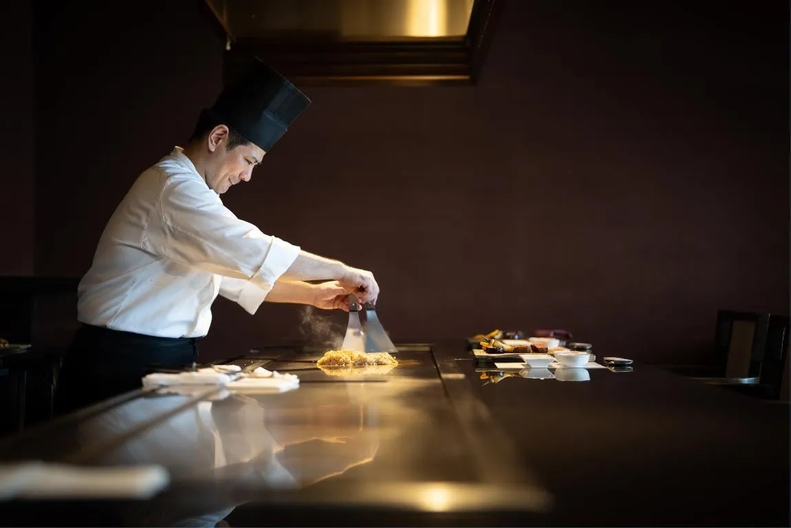 カウンター越しに調理を行う鉄板焼きのシェフ