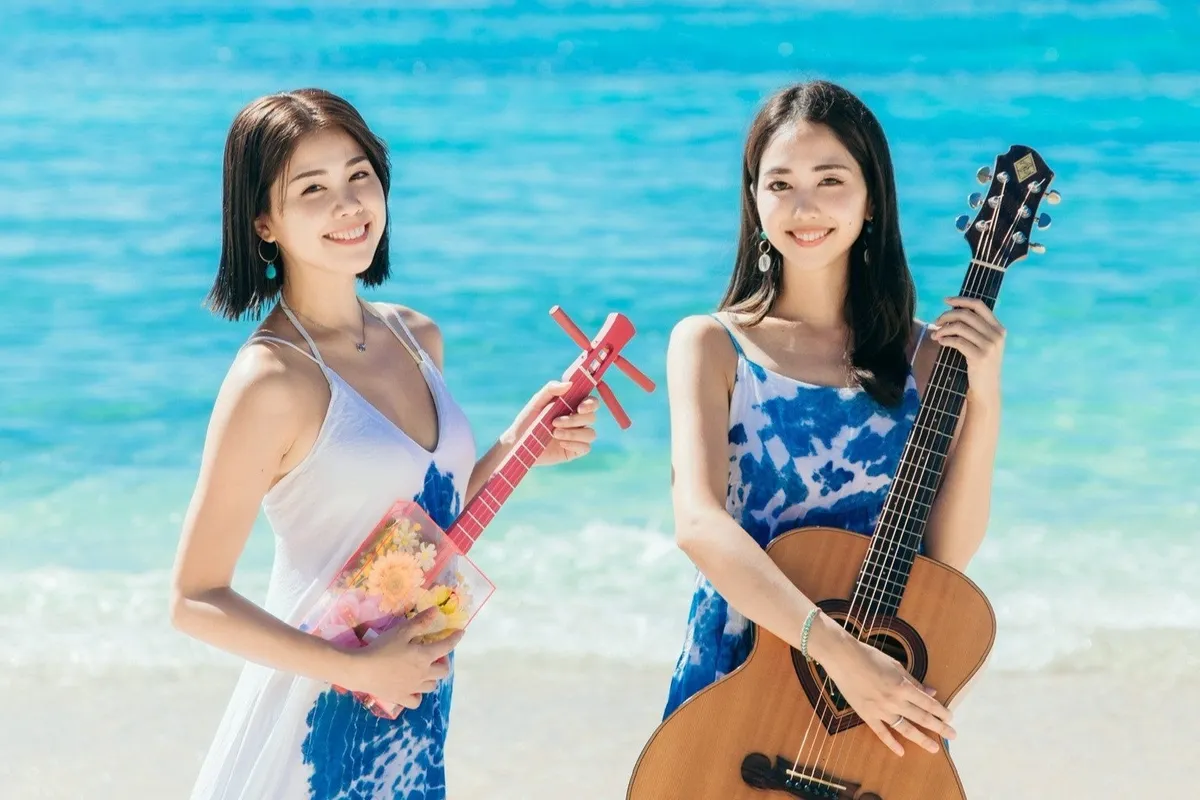 透き通る海を背景に笑顔で楽器を構える二人の女性デュオ