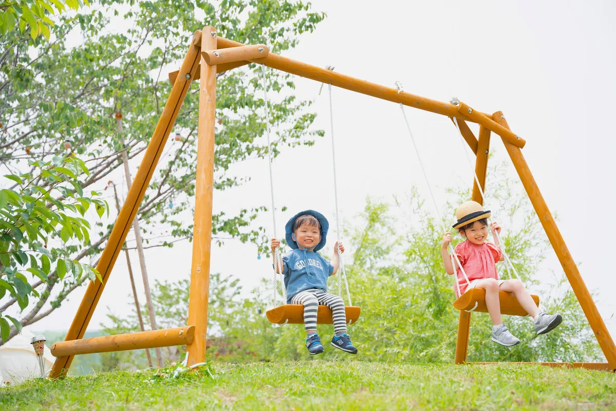 緑豊かな屋外で木製のブランコを楽しむ笑顔の子供たち