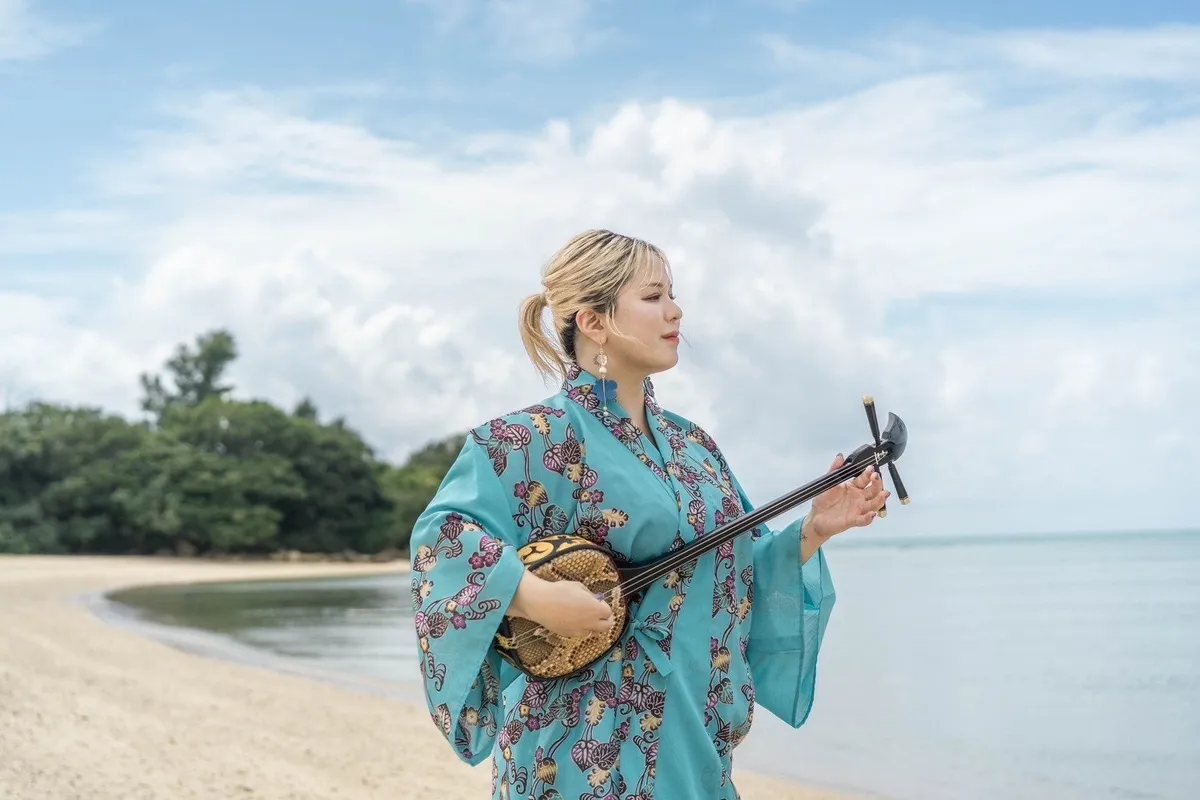 青い海をバックに砂浜で三線を奏でる女性アーティスト
