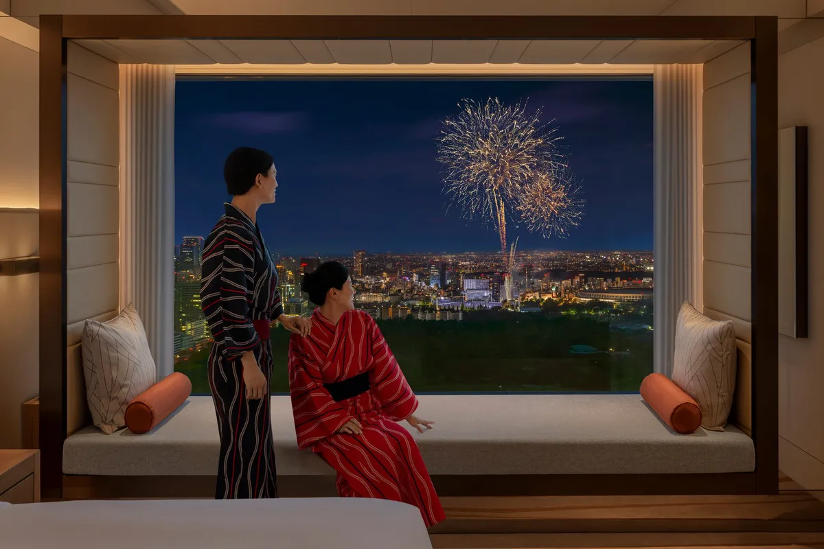 窓際のデイベッドから花火を眺める浴衣姿の二人