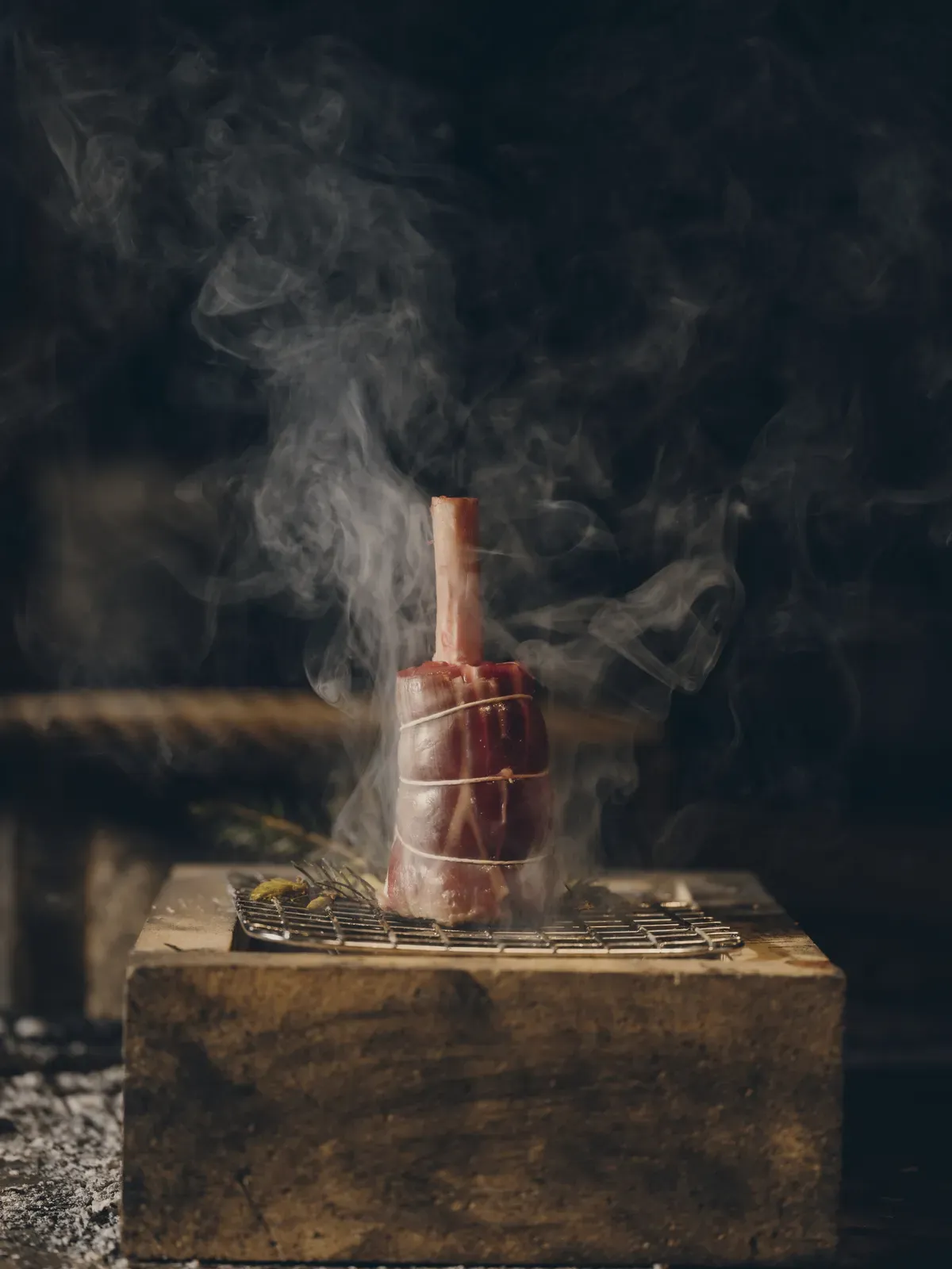 石の上で薪火によって調理される、立ち上る煙が印象的な肉料理