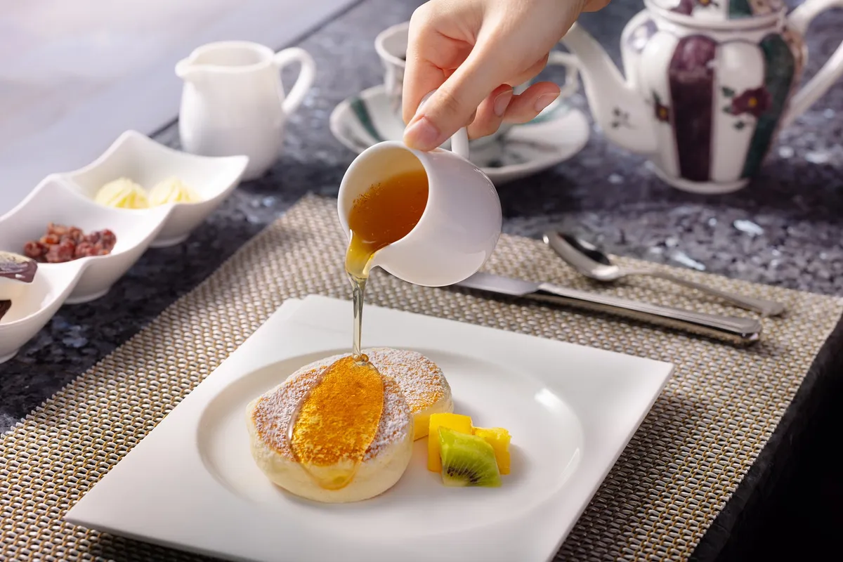 白い皿に盛られたパンケーキにシロップをかける様子
